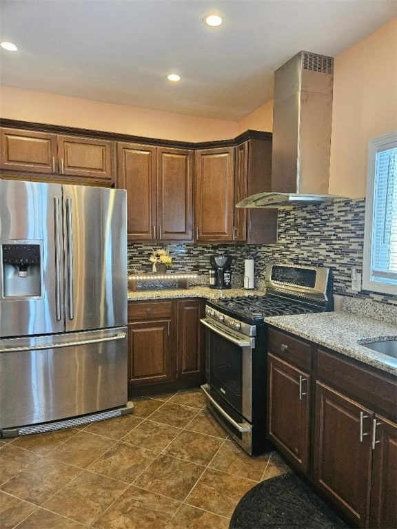 kitchen with gas range, stainless steel refrigerator with ice dispenser, decorative backsplash, wall chimney exhaust hood, and light stone countertops