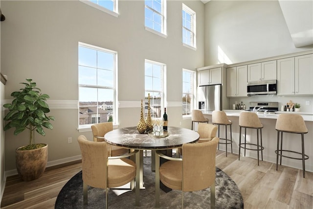 dining space with a towering ceiling, light wood-type flooring, and a wealth of natural light