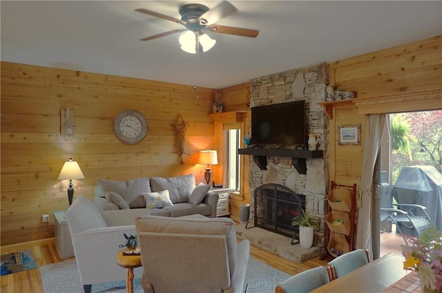 living room with wood walls, ceiling fan, light hardwood / wood-style floors, and a stone fireplace