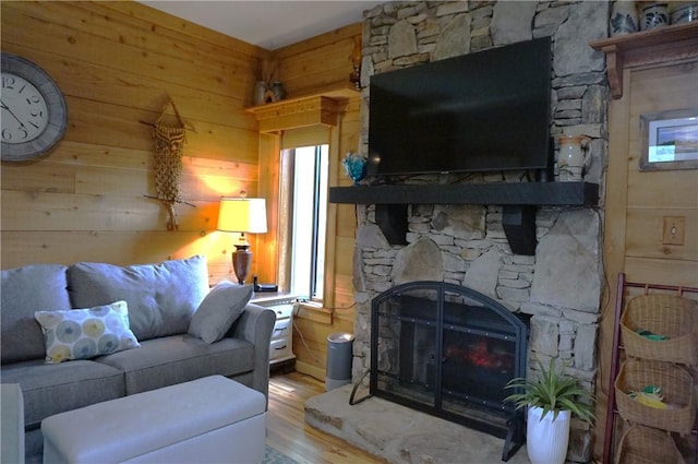 living room with hardwood / wood-style flooring, wooden walls, and a stone fireplace