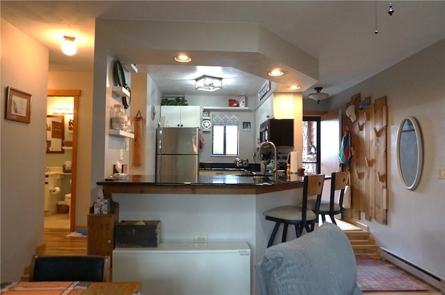 kitchen with sink, white cabinetry, kitchen peninsula, stainless steel fridge, and baseboard heating