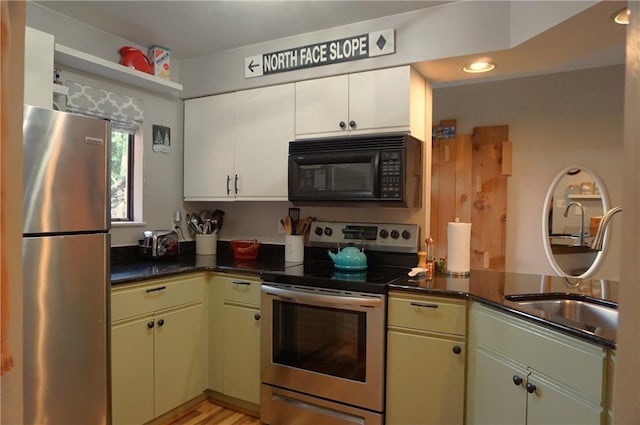 kitchen featuring dark stone countertops, appliances with stainless steel finishes, light hardwood / wood-style floors, sink, and white cabinetry