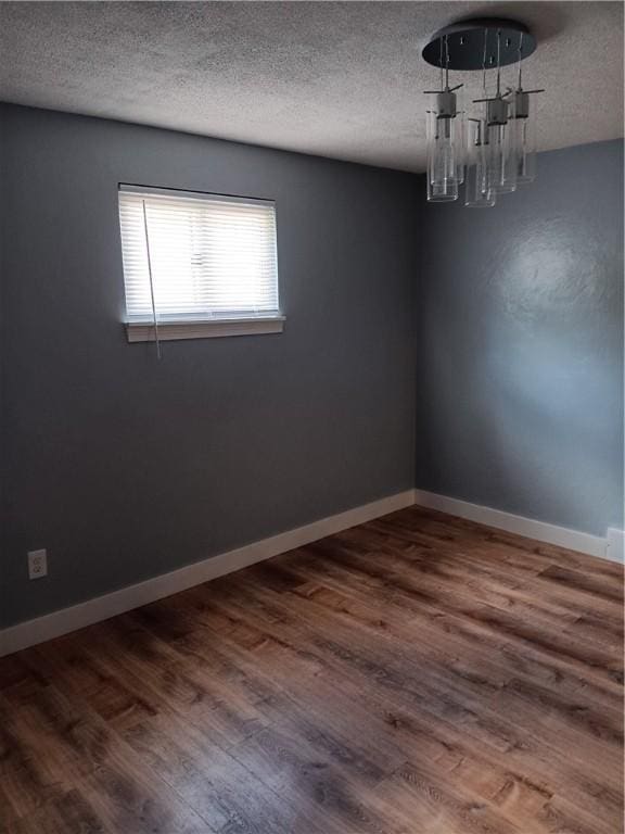 spare room featuring a chandelier, wood-type flooring, and a textured ceiling