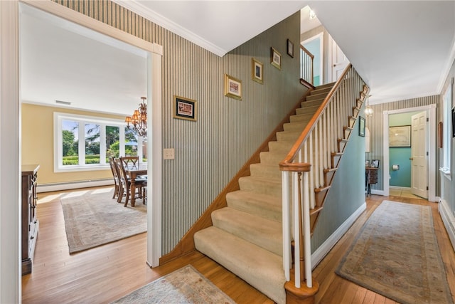 stairway featuring a baseboard heating unit, ornamental molding, an inviting chandelier, and light wood-type flooring