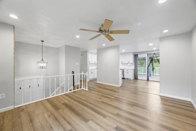 unfurnished living room with light wood-type flooring and ceiling fan with notable chandelier