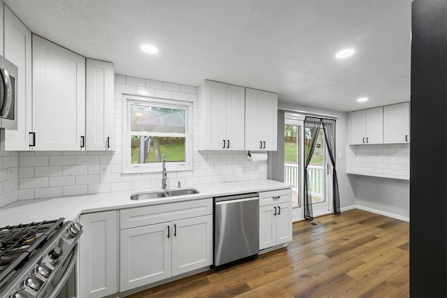 kitchen with white cabinets, stainless steel appliances, backsplash, hardwood / wood-style floors, and sink