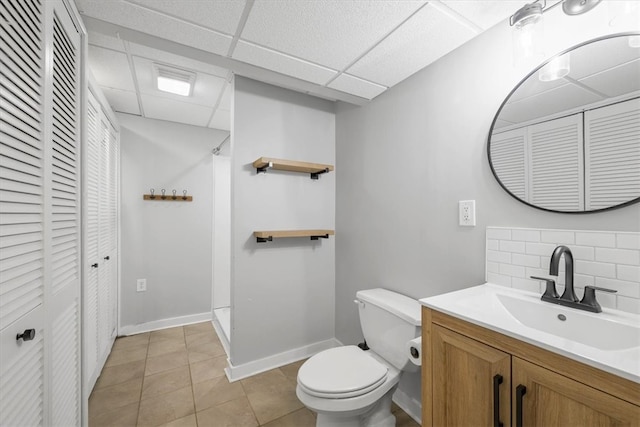 bathroom with a paneled ceiling, toilet, tasteful backsplash, tile flooring, and vanity