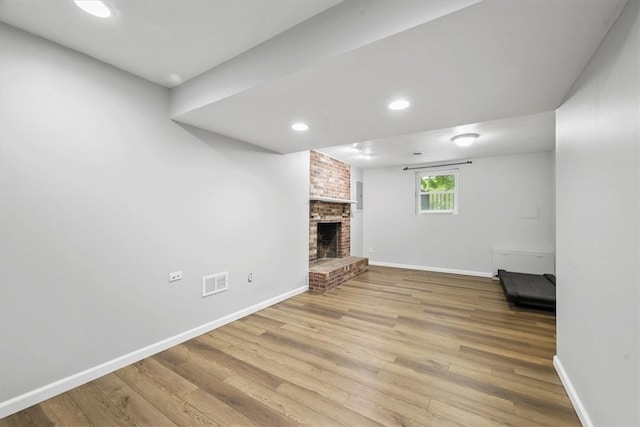 unfurnished living room with light hardwood / wood-style floors, a fireplace, and brick wall