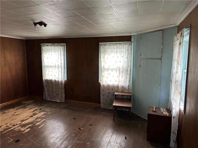 spare room with crown molding, dark wood finished floors, wooden walls, and baseboards