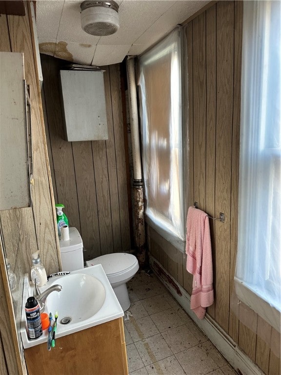 bathroom with a paneled ceiling, toilet, tile flooring, wooden walls, and vanity