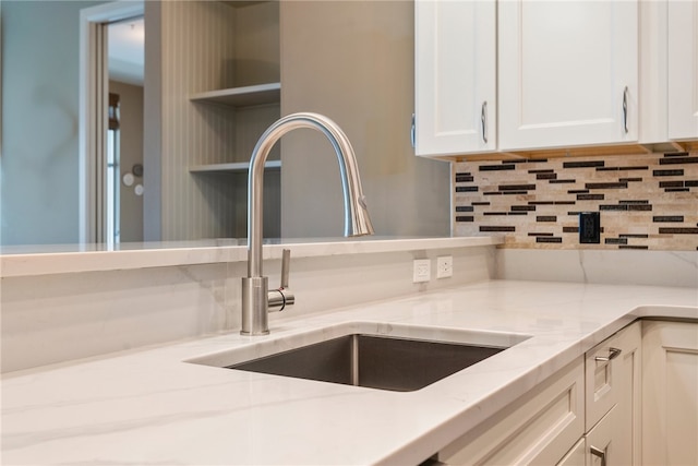 interior space featuring sink, light stone countertops, backsplash, and white cabinetry