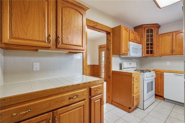 kitchen featuring tile counters, white appliances, light tile floors, and tasteful backsplash