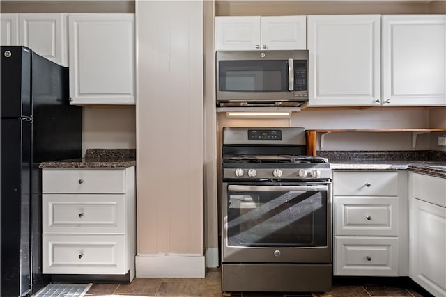 kitchen with appliances with stainless steel finishes, dark stone countertops, wooden walls, and white cabinets