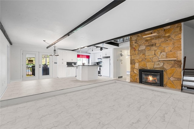 unfurnished living room with beamed ceiling, a stone fireplace, light tile flooring, and french doors