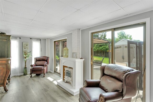 living area with brick wall, a wood stove, light wood-type flooring, and crown molding