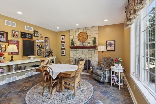 dining area featuring a stone fireplace and dark tile floors