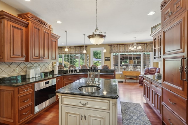 kitchen featuring an island with sink, stainless steel oven, pendant lighting, and dark wood-type flooring