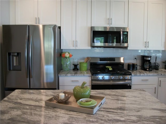 kitchen featuring tasteful backsplash, light stone countertops, appliances with stainless steel finishes, and white cabinets