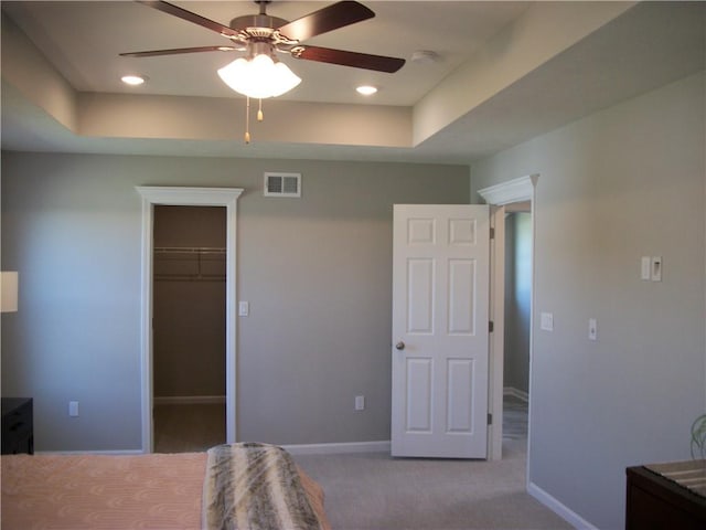 carpeted bedroom featuring ceiling fan, a tray ceiling, a closet, and a spacious closet