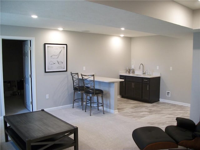 bar with dark brown cabinetry, sink, and light colored carpet