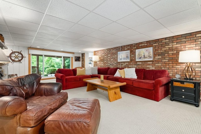 carpeted living room with a paneled ceiling and brick wall