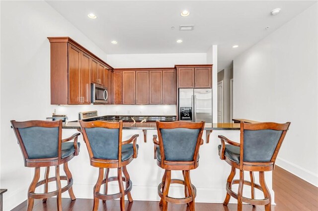 kitchen with a breakfast bar area, wood-type flooring, kitchen peninsula, and stainless steel appliances