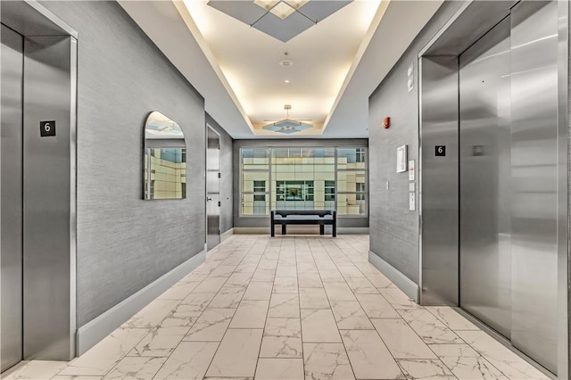 hallway with elevator and a tray ceiling