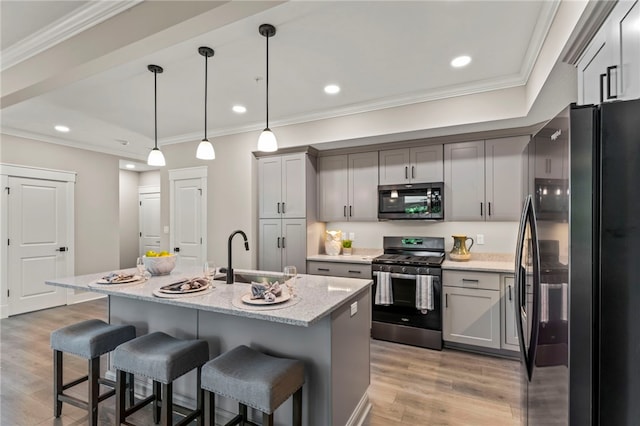 kitchen with an island with sink, stainless steel appliances, light hardwood / wood-style floors, decorative light fixtures, and sink