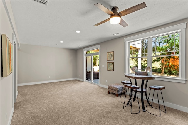 living area with light carpet, a textured ceiling, and ceiling fan