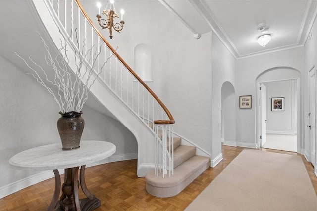 entrance foyer with a notable chandelier, a towering ceiling, crown molding, and parquet floors