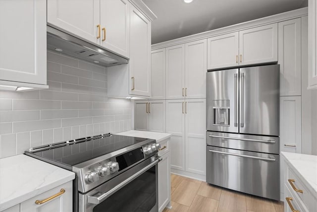 kitchen with white cabinets, stainless steel appliances, light stone counters, and ventilation hood