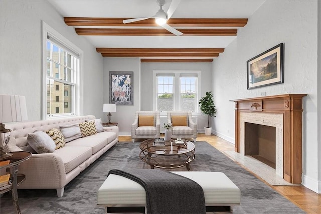 living room with ceiling fan, dark wood-type flooring, a premium fireplace, and beamed ceiling