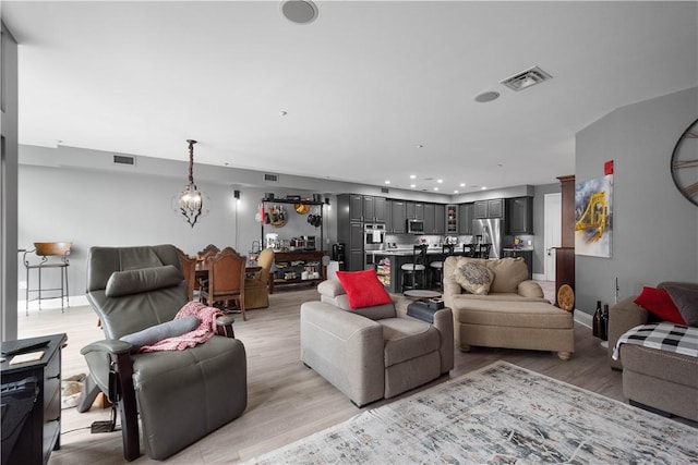 living room featuring light wood-type flooring, baseboards, visible vents, and a chandelier