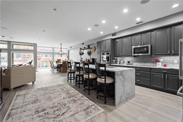 kitchen featuring light wood-type flooring, a kitchen island with sink, stainless steel appliances, decorative backsplash, and a kitchen breakfast bar