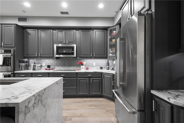 kitchen with stainless steel appliances, decorative backsplash, sink, light stone countertops, and light hardwood / wood-style flooring