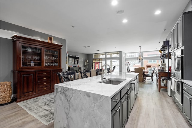 kitchen featuring sink, light wood-type flooring, a kitchen island with sink, and light stone countertops