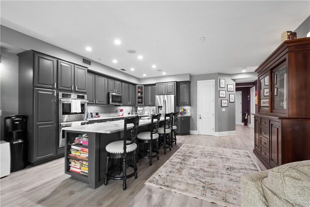 kitchen featuring a kitchen island, light wood-type flooring, tasteful backsplash, and stainless steel appliances