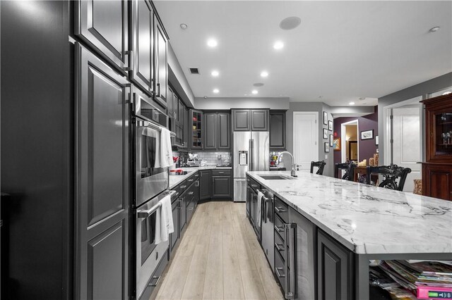 kitchen featuring tasteful backsplash, light wood-type flooring, an island with sink, sink, and light stone counters