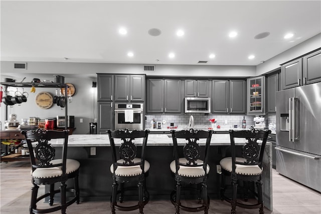 kitchen featuring a center island with sink, appliances with stainless steel finishes, light wood-type flooring, and gray cabinetry