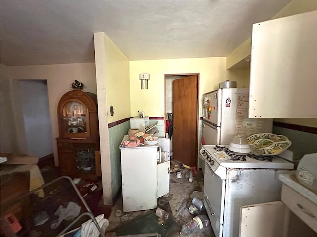 kitchen featuring white gas range, refrigerator, and white cabinets