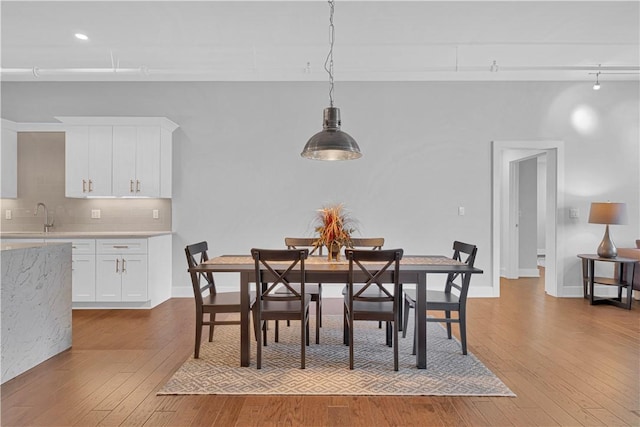 dining area featuring rail lighting, sink, and light hardwood / wood-style flooring