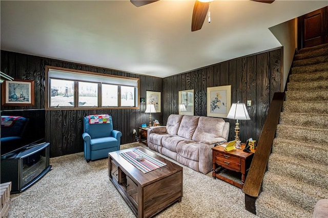 carpeted living room with ceiling fan and wood walls