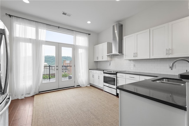 kitchen with wall chimney exhaust hood, sink, white cabinetry, appliances with stainless steel finishes, and decorative backsplash