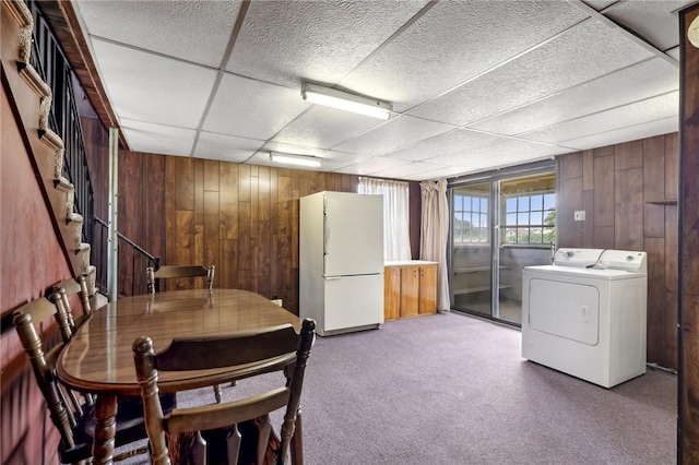 unfurnished dining area featuring carpet floors, a drop ceiling, and wood walls