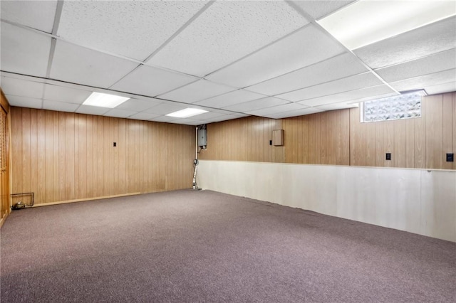 basement featuring a drop ceiling, carpet, and wooden walls