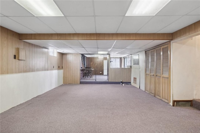 basement featuring a paneled ceiling, carpet flooring, and wooden walls