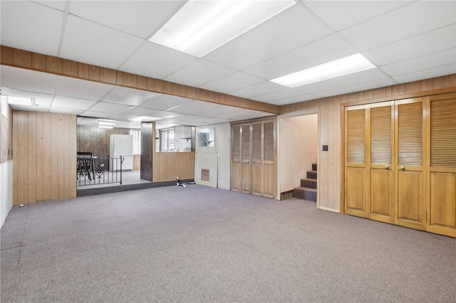 basement with carpet, a paneled ceiling, wood walls, and white fridge