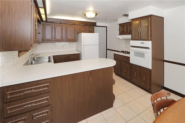 kitchen with kitchen peninsula, sink, white appliances, light tile patterned flooring, and dark brown cabinets