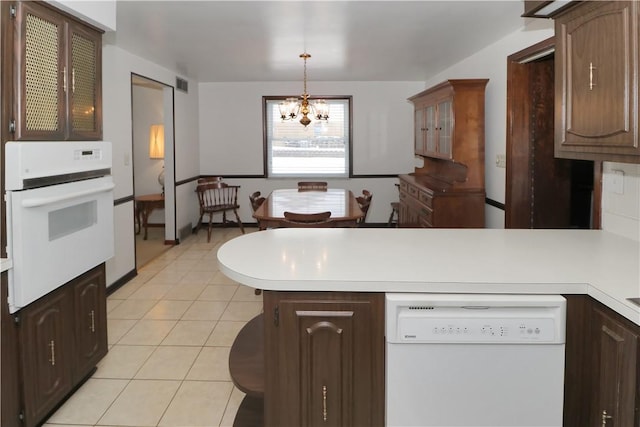 kitchen featuring kitchen peninsula, white appliances, dark brown cabinets, hanging light fixtures, and a chandelier