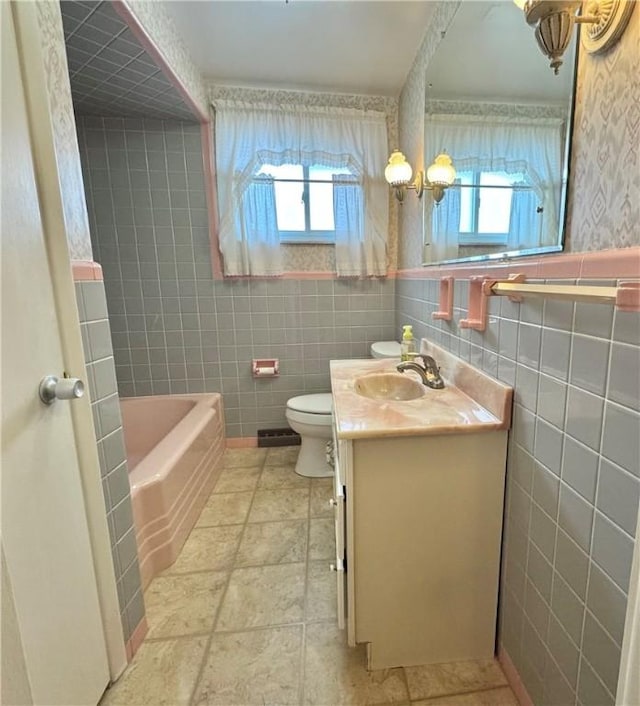 bathroom with toilet, vanity, tile walls, and a bath